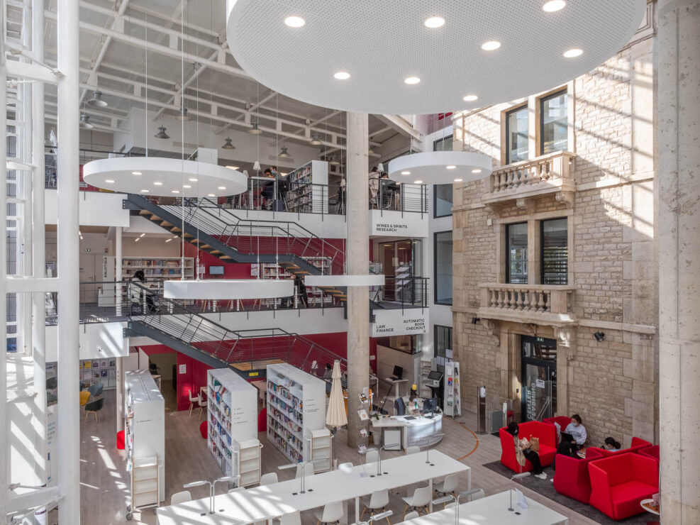 View of the main atrium of the Burgundy School of Business Learning Centre in Dijon, France. To the right of the multistory space, the former 1900s facade of the school can be seen.