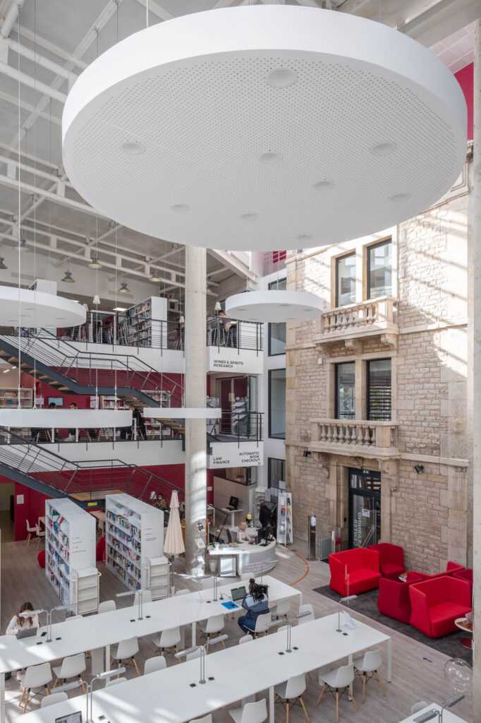 View of the main atrium of the Burgundy School of Business Learning Centre in Dijon, France. To the right of the multistory space, the former 1900s facade of the school can be seen.