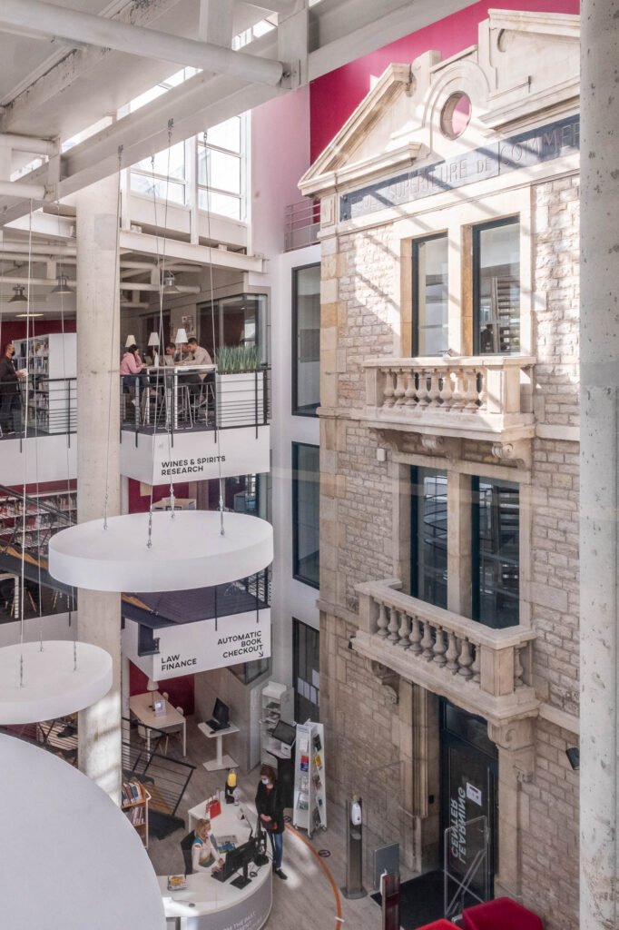 View of the main atrium of the Burgundy School of Business Learning Centre in Dijon, France. To the right of the multistory space, the former 1900s facade of the school can be seen.