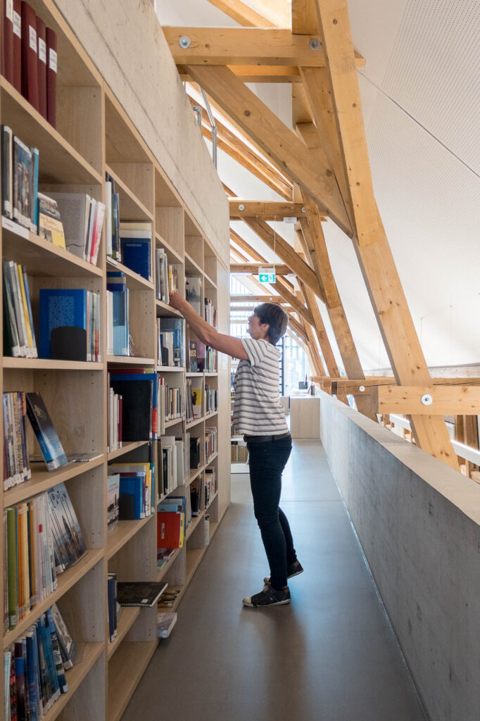 A librarian is seen reaching to a bookshelf.