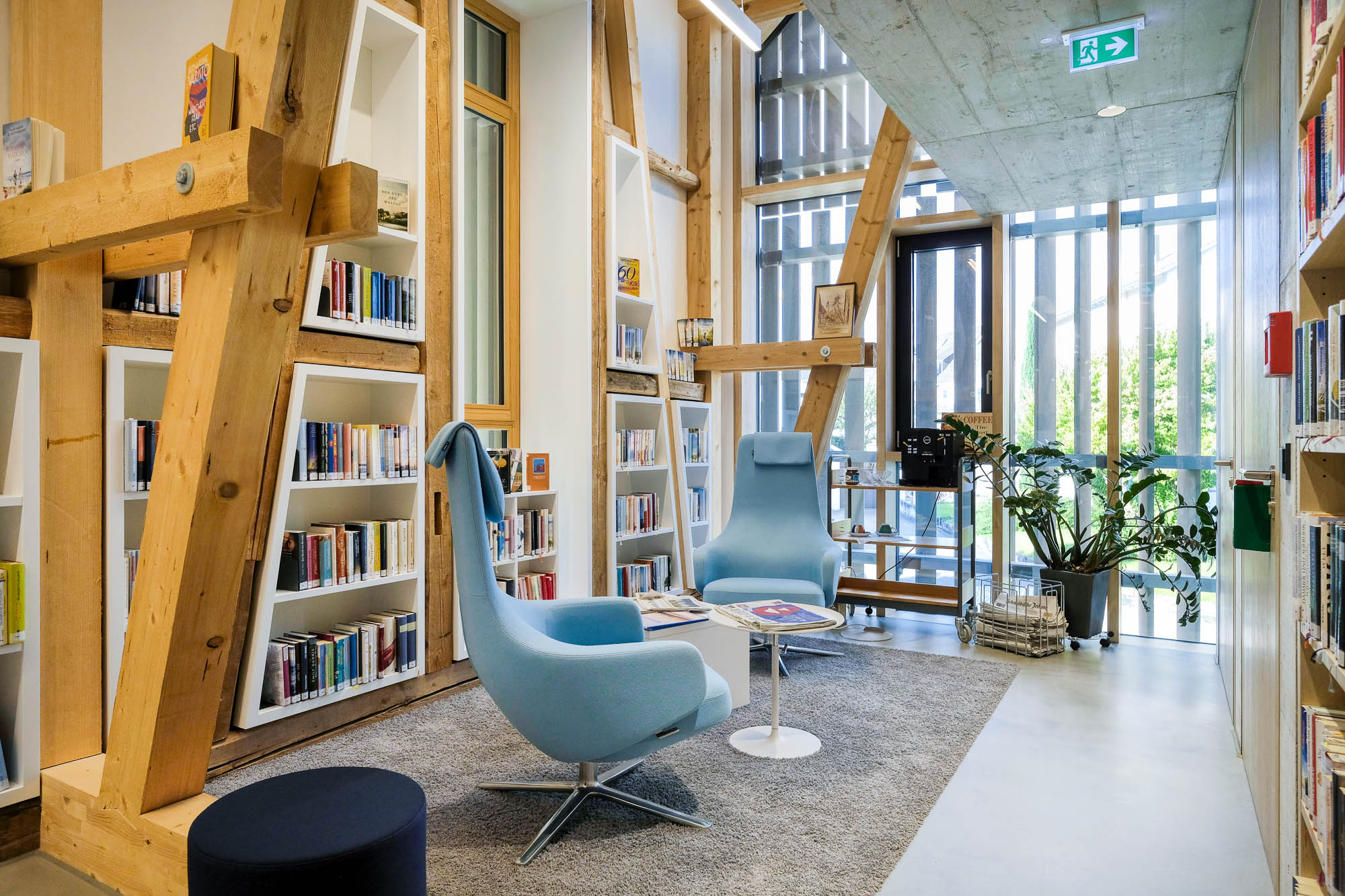Library interior showing a reading area furnished with two pale blue comforters, low tables and coffee making equipment. The walls show original half-timbered framework with bookcases built inbetween.