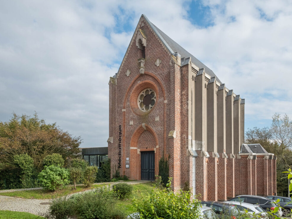 Exterior view of a brick chapel converted to a library. It is a tall, narrow neo-gothic building, with a rose window on top of a vaulted door. A sideways sign bearing the word "Médiathèque" is affixed to the facade.
