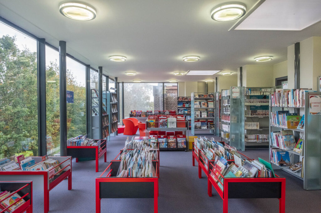 Interior view of a modern library. It is a rectangular, glass-fronted room with colourful bookshelves.
