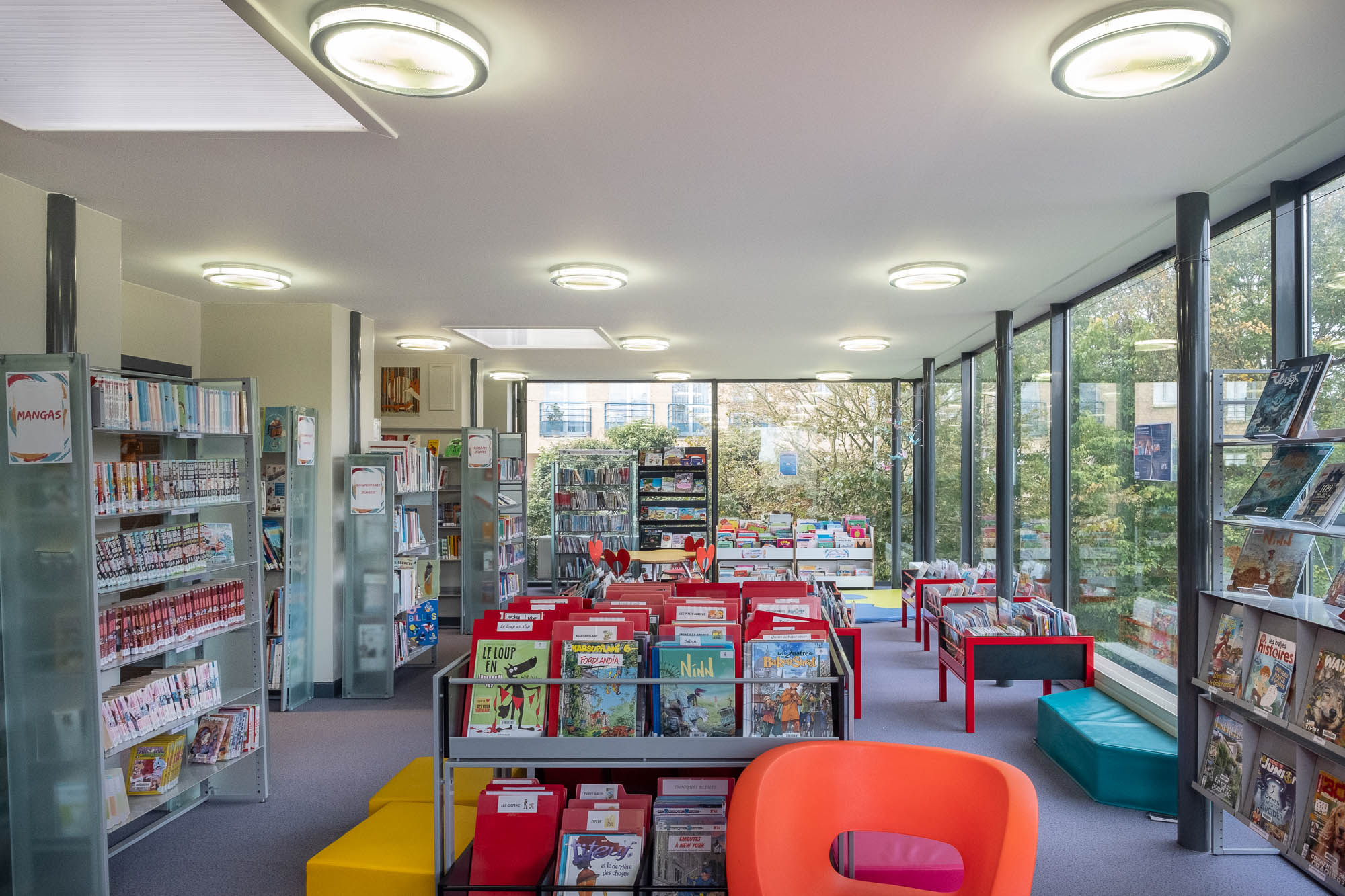 Interior view of a modern library. It is a rectangular, glass-fronted room with colourful bookshelves.