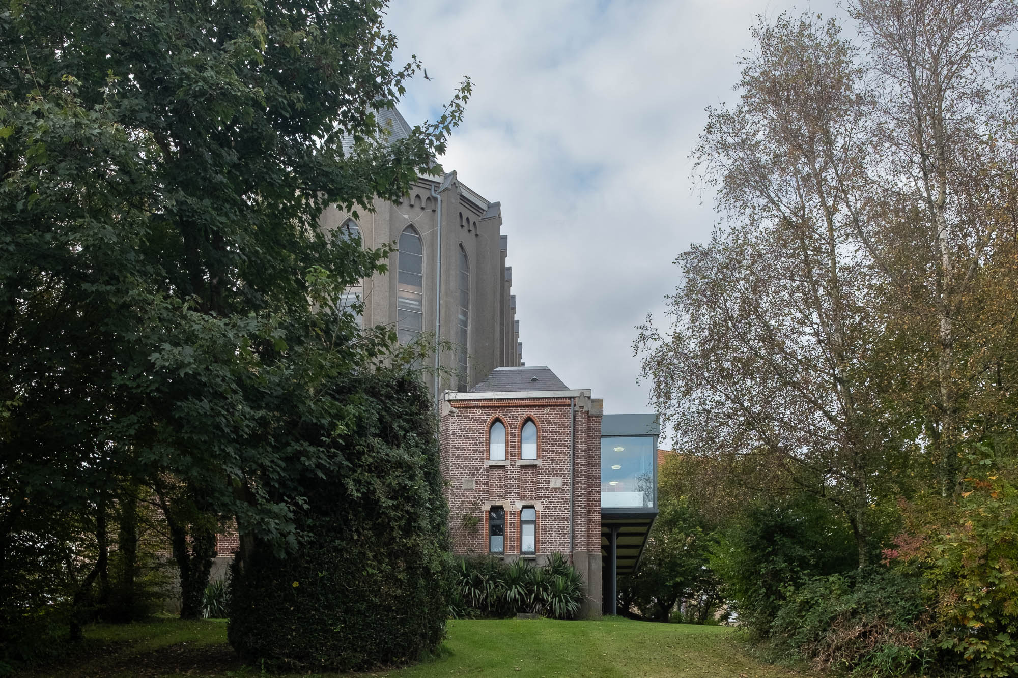 Exterior view of a brick chapel converted to a library peeking through tall trees.