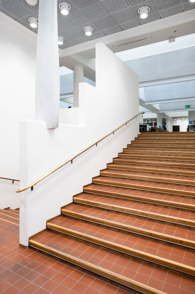 Interior of a modern library, stairs of red tile with a wooden edge.