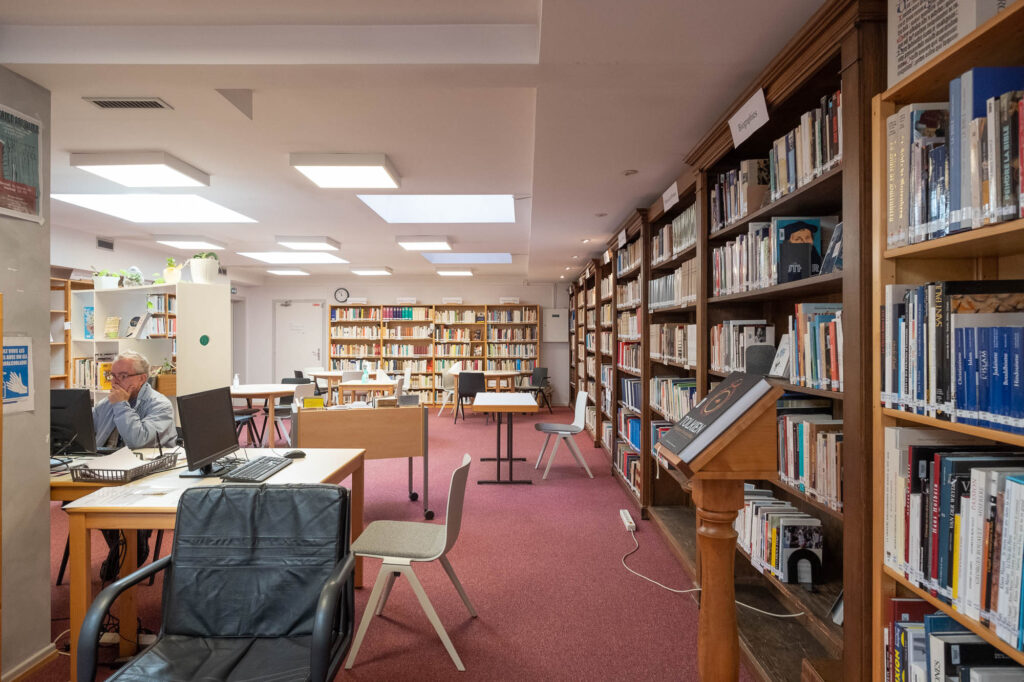 Interior of a library reading room. It is a subterranean room lighted by skylight, with pink/magenta carpet and wooden bookshelves.