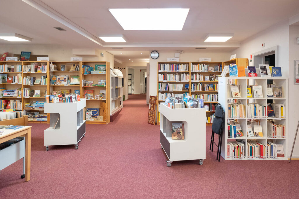 Interior of a library reading room. It is a subterranean room lighted by skylight, with pink/magenta carpet and wooden bookshelves.