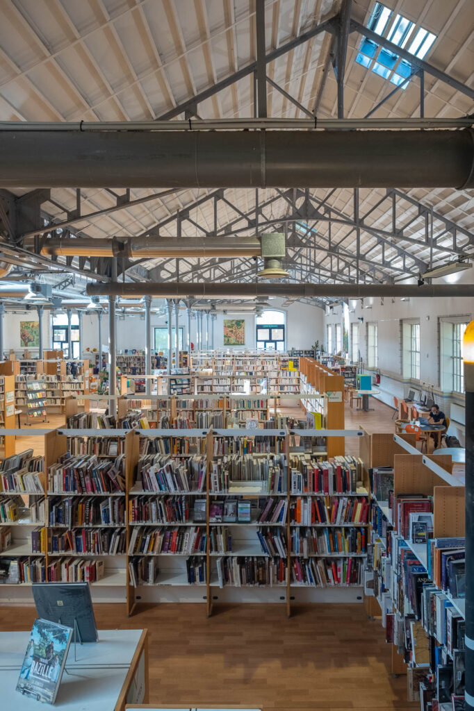 Interior of an industrial space converted into a library. The space is filled with modern wood and metal bookshelves.