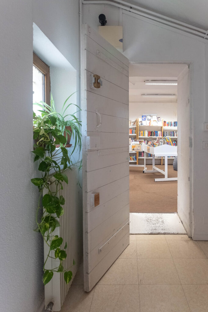 Interior of an old bastide house transformed into a library, showing a doorway with a whitewashed wooden door and a window.