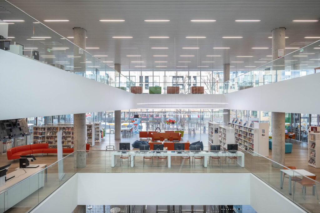 Interior of a contemporary library, showing an atrium surrounded by levels of bookshelves, tables and chairs.