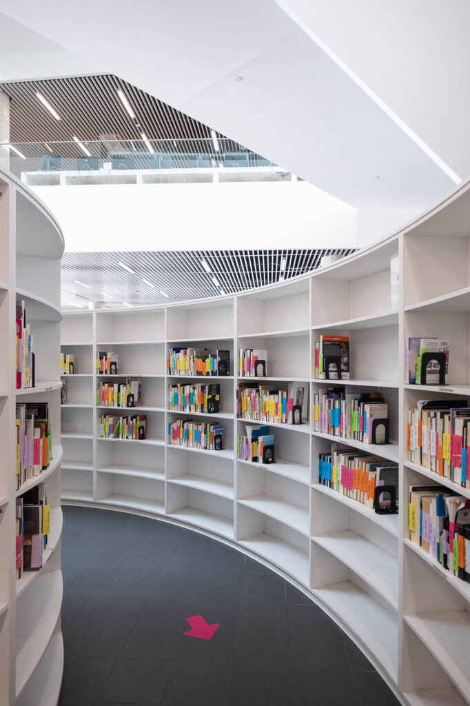 Interior of a contemporary library, showing a curved wall of bookshelves. A pink arrow is drawn on the floor.