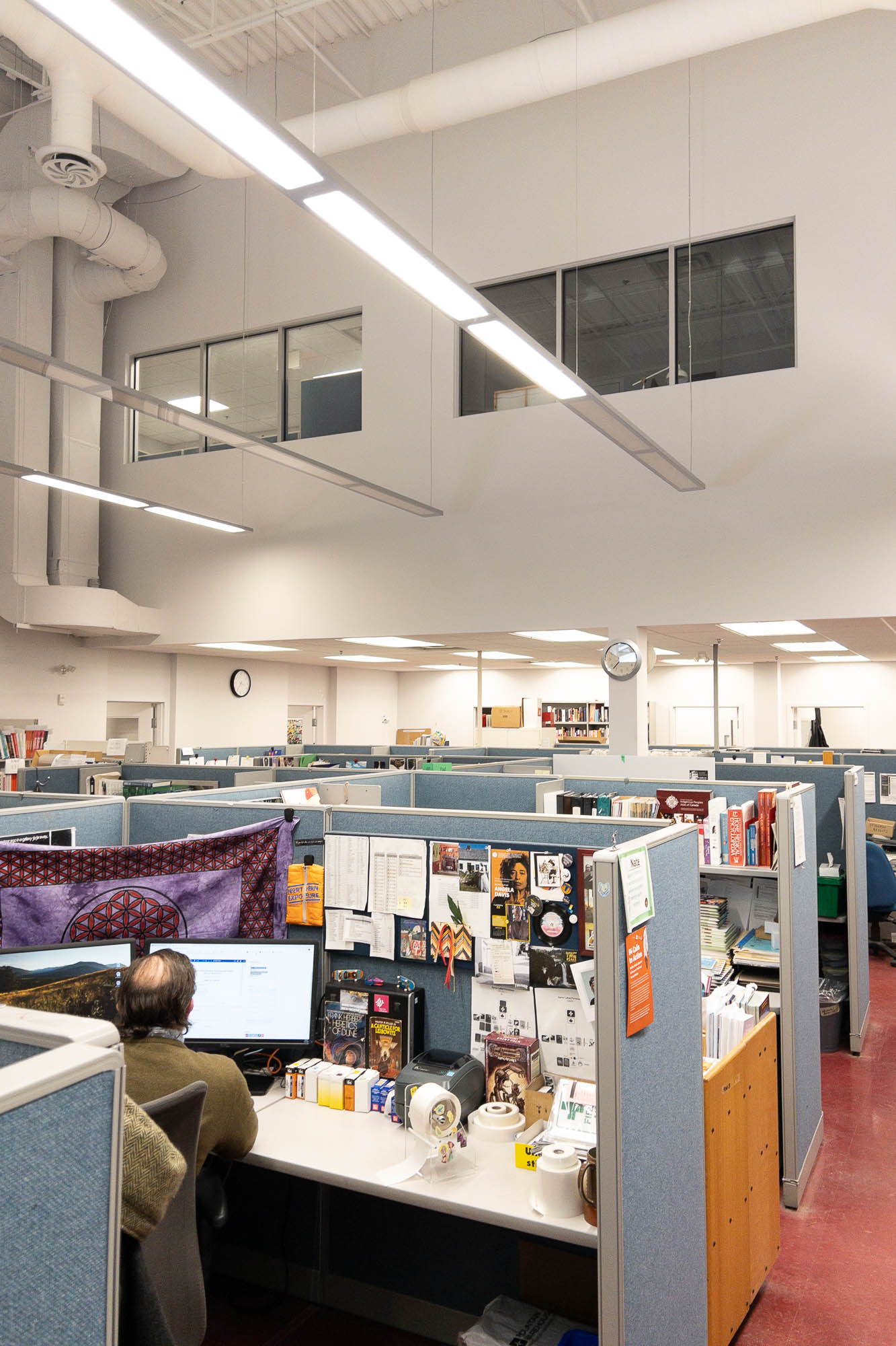 Interior of a library backoffice area. Rectangular windows are seen above a series of cubicles, hinting at their former use as projection booth.