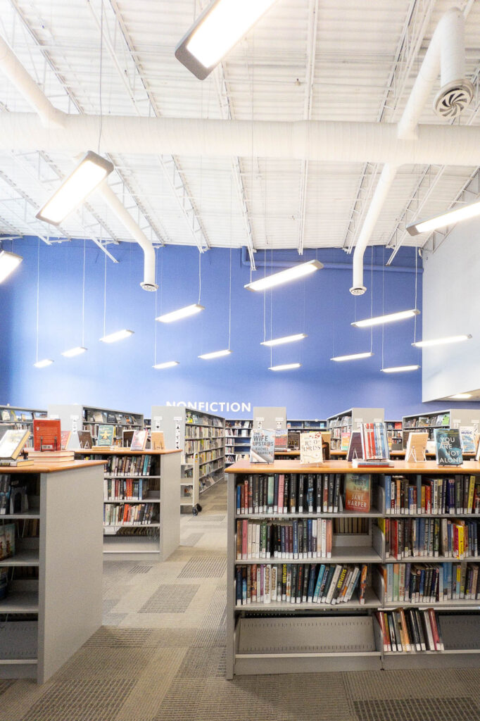 Interior of a contemporary public library with shelves before a blue wall with the word "Nonfiction" printed on it.