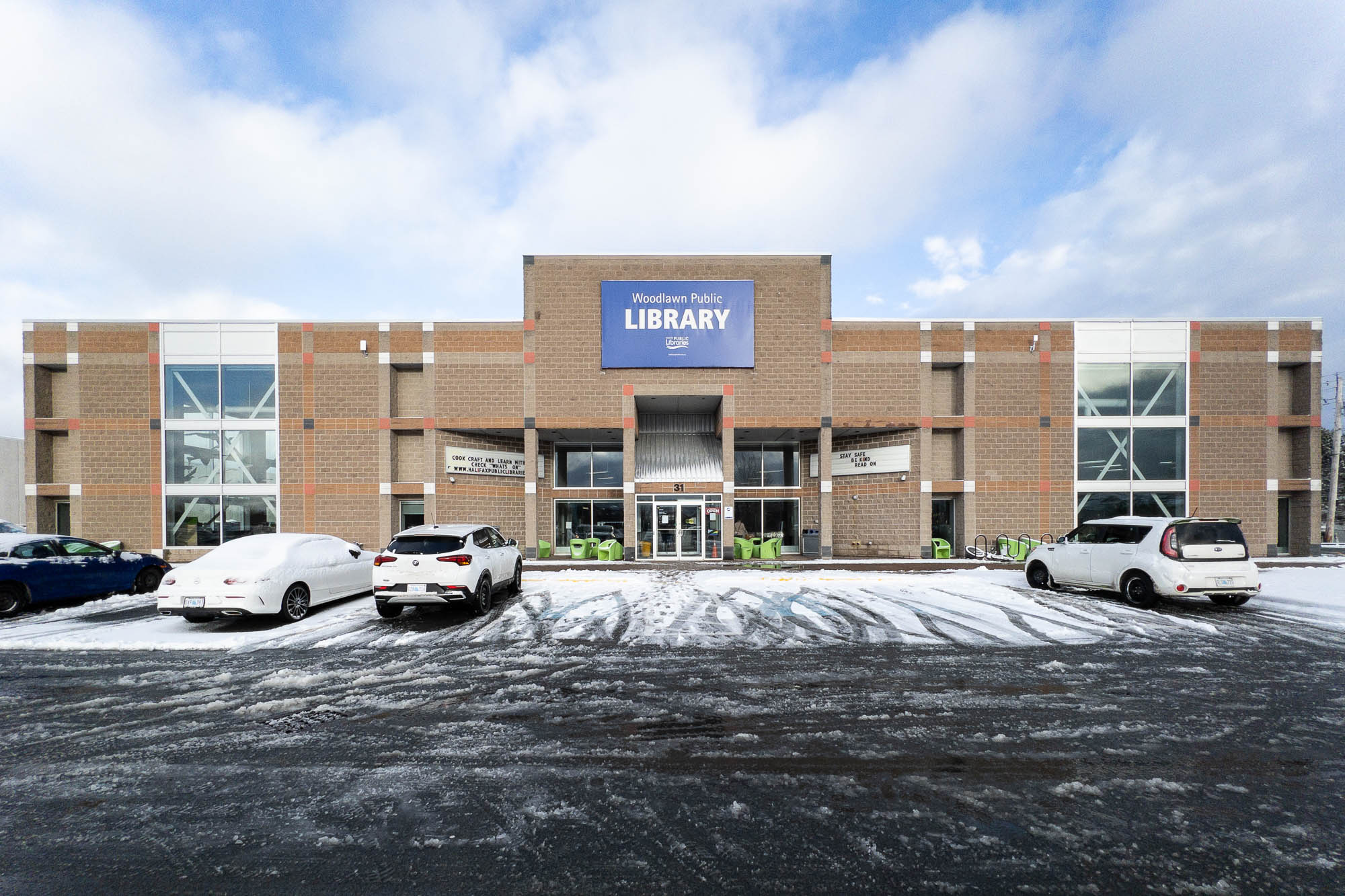 Exterior of a former mall movie multiplex converted into a library. It is a symmetrical brick Postmodern building. A blue sign with the words "Woodlawn Public Library" stands above the entrance. Cars are parked at the front. There is snow on the ground.