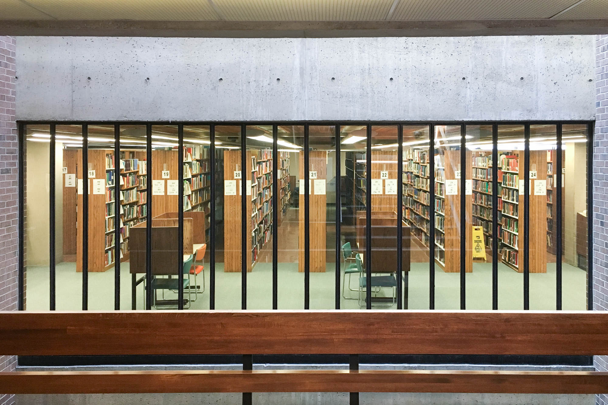 Interior of a brick modernist library building through a wall of rectangular windows.