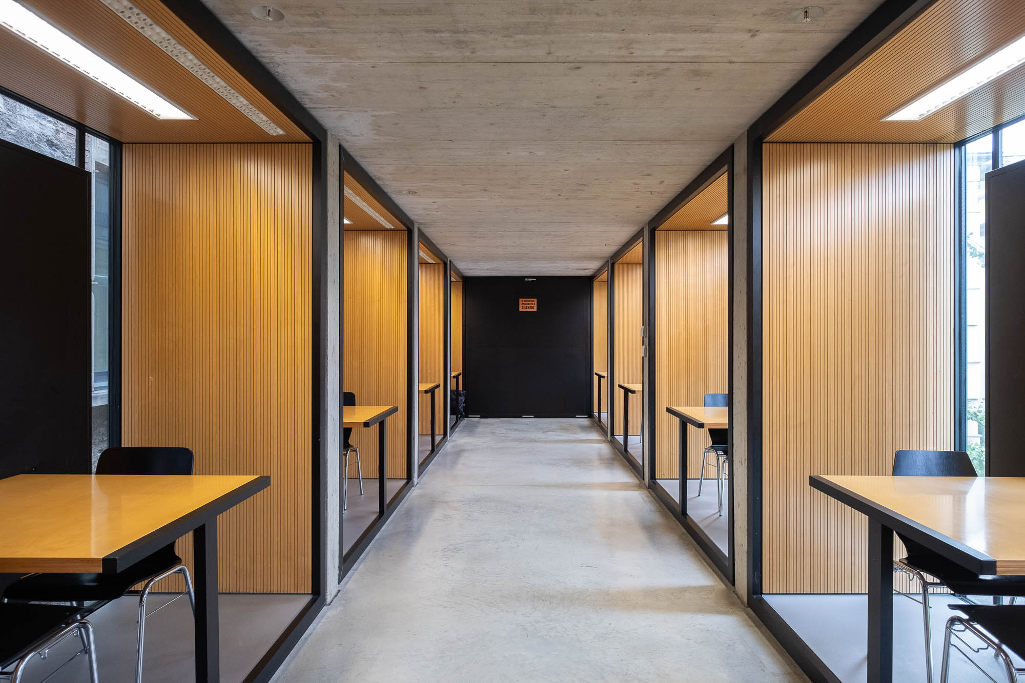 Contemporary library interior, showing a row of square cubicles enclosed by wood lattice panels on either side of a corridor.