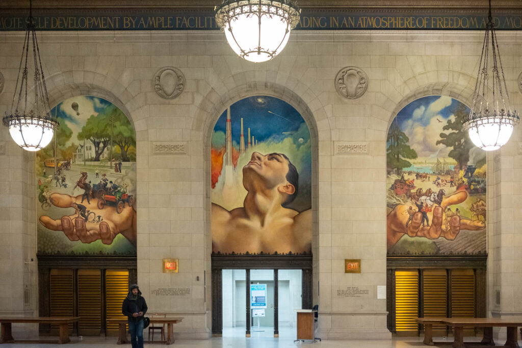 Interior of a Beaux-Arts library building, showing a large mural depicting the bust of a man holding allegories of scientific achievements.