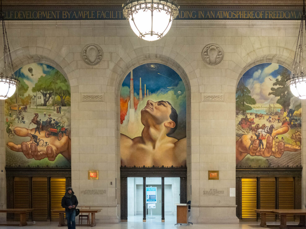 Interior of a Beaux-Arts library building, showing a large mural depicting the bust of a man holding allegories of scientific achievements.
