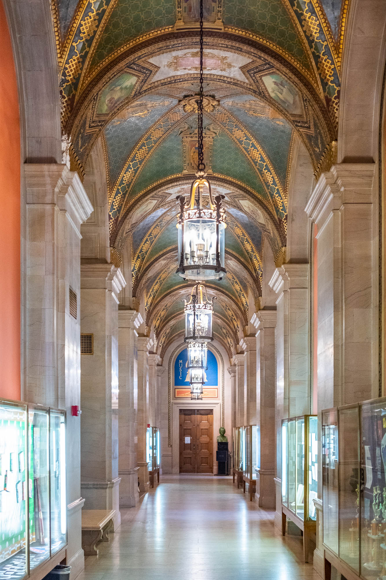 Interior of a richly decorated Beaux-Arts library corridor, with gilded and coloured vaulted ceilings and cylindrical chandeliers.