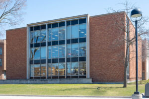 Exterior of a brick modernist library, a symmetrical rectangular building with a bay of concrete-framed windows to the centre.