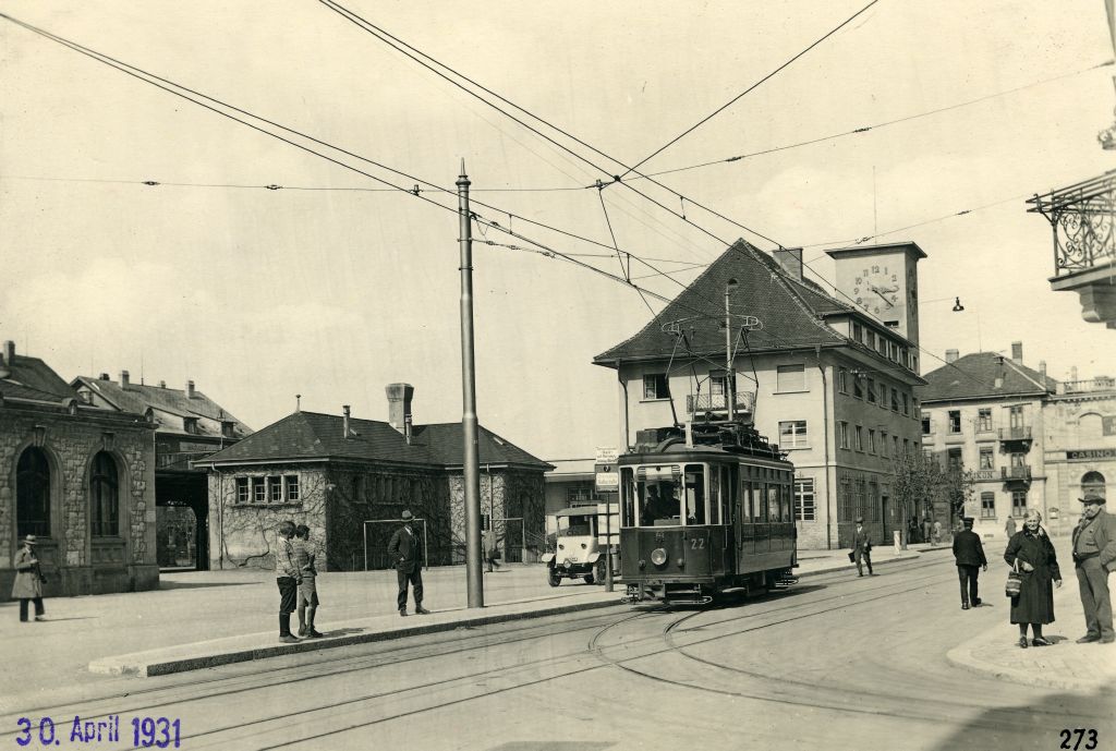 Archival black and white photograph of a turning electric tramway. In the background is an early modern post office with a square clock tower.