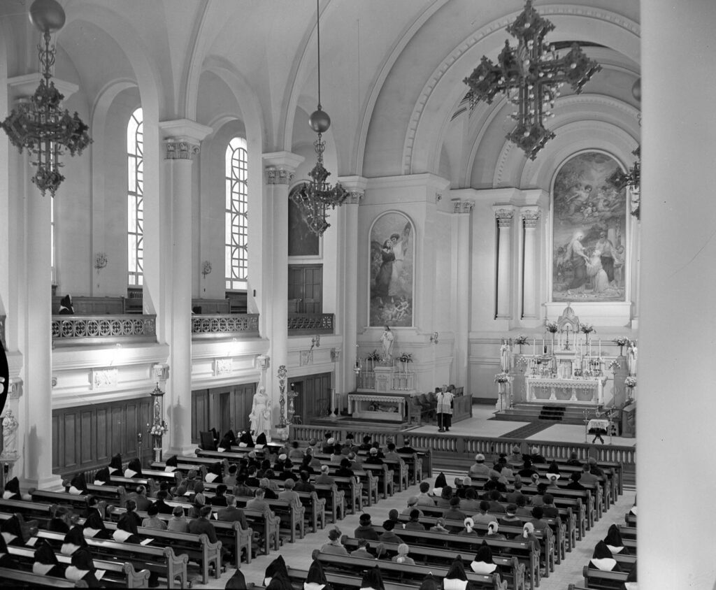 Archival black and white image of a religious ceremony in a Neoclassical chapel.