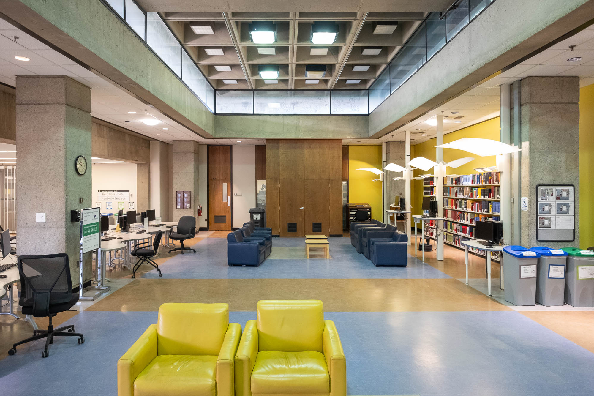 Interior of a Brutalist library with waffle ceiling and large concrete columns. The space has been recently refurbished with colourful walls, indirect lighting and colourful sofas.