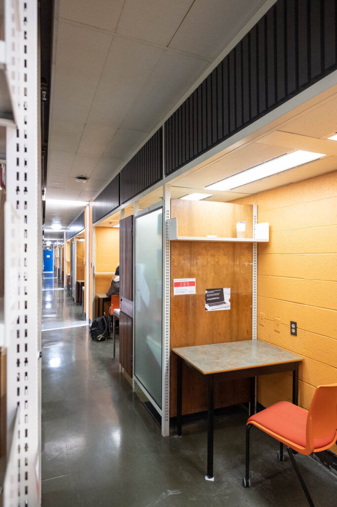 View of a corridor inside a library, with work cubicles to the right. A person can be seen occupying one of the cubicles.