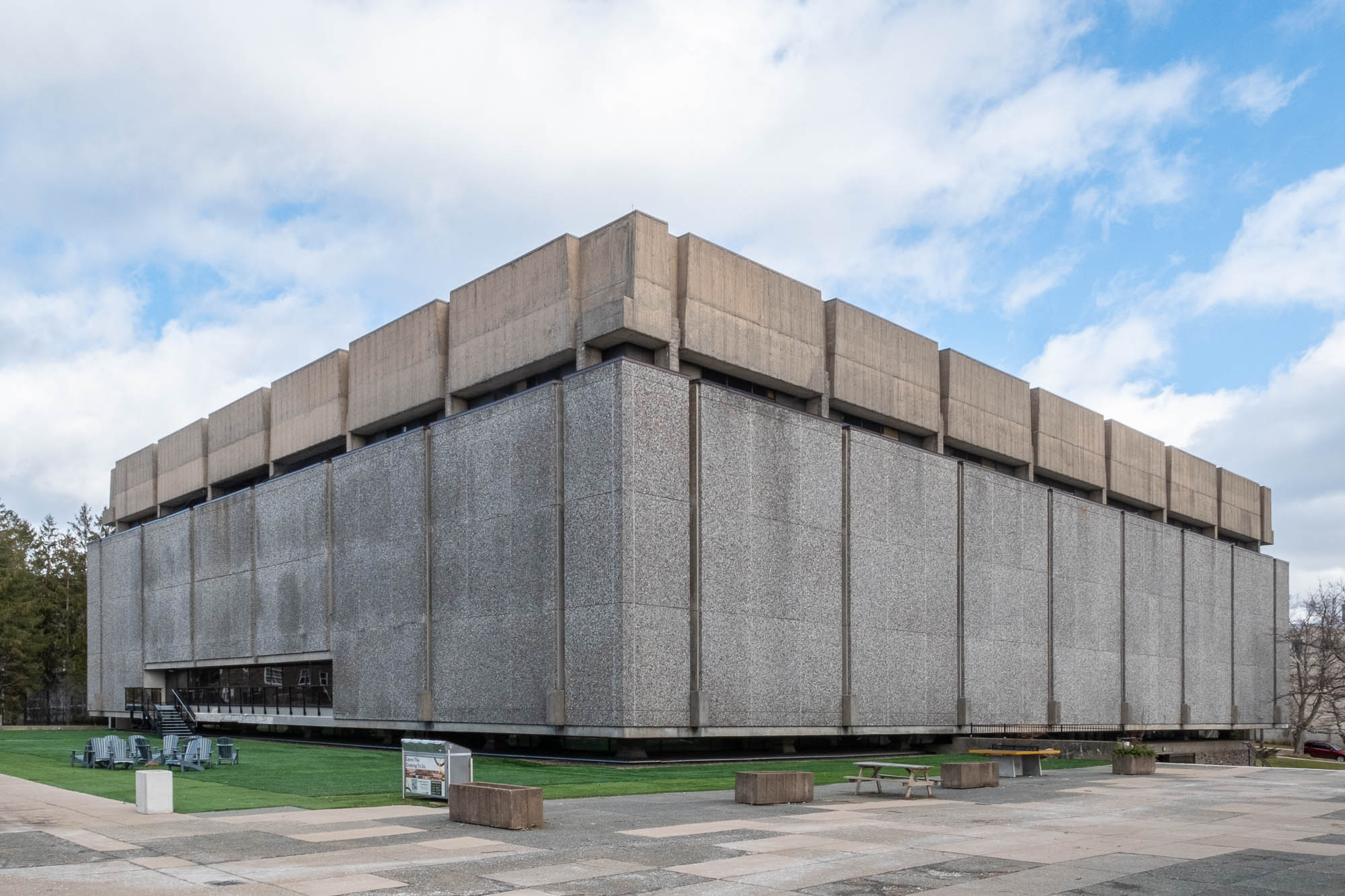 Exterior of a Brutalist library with a facade of large textured concrete panels between which are narrow vertical slit windows.