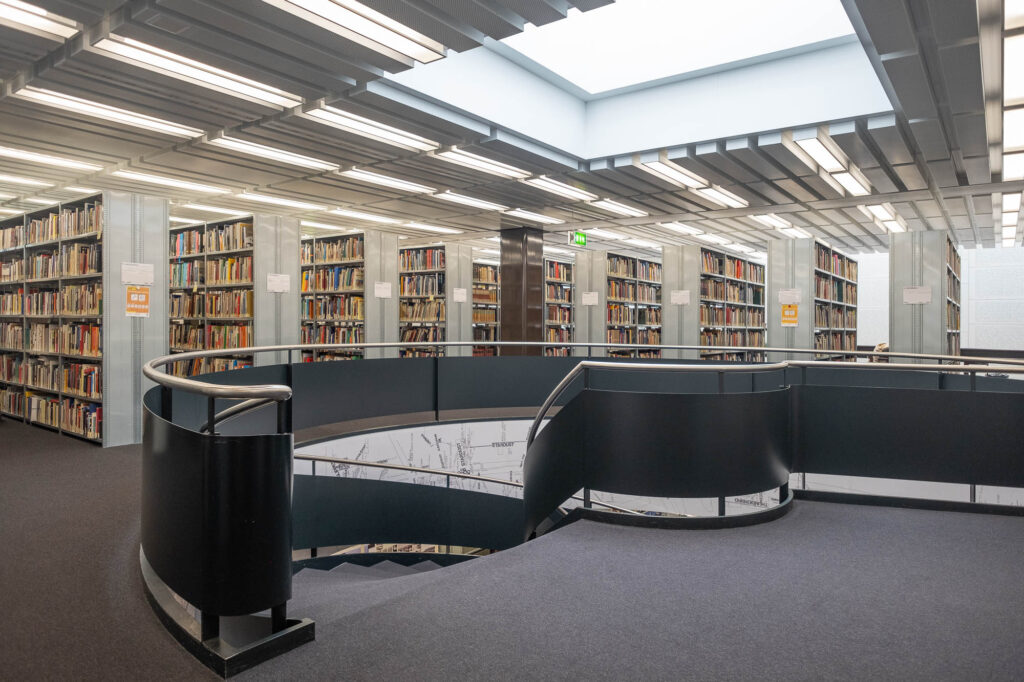 Interior of a library, with a spiral staircase at the front and metal bookshelves at the back.