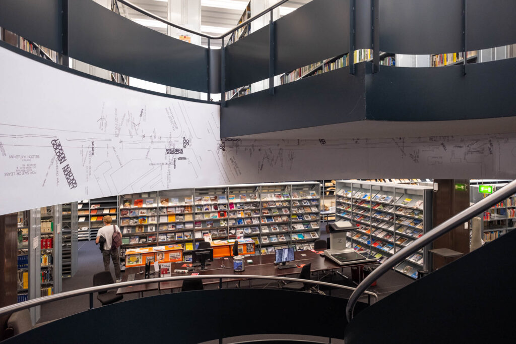 Interior of a library, viewed from the interior of a spiral staircase. Bookshelves can be seen on the floors above and below the stairs.