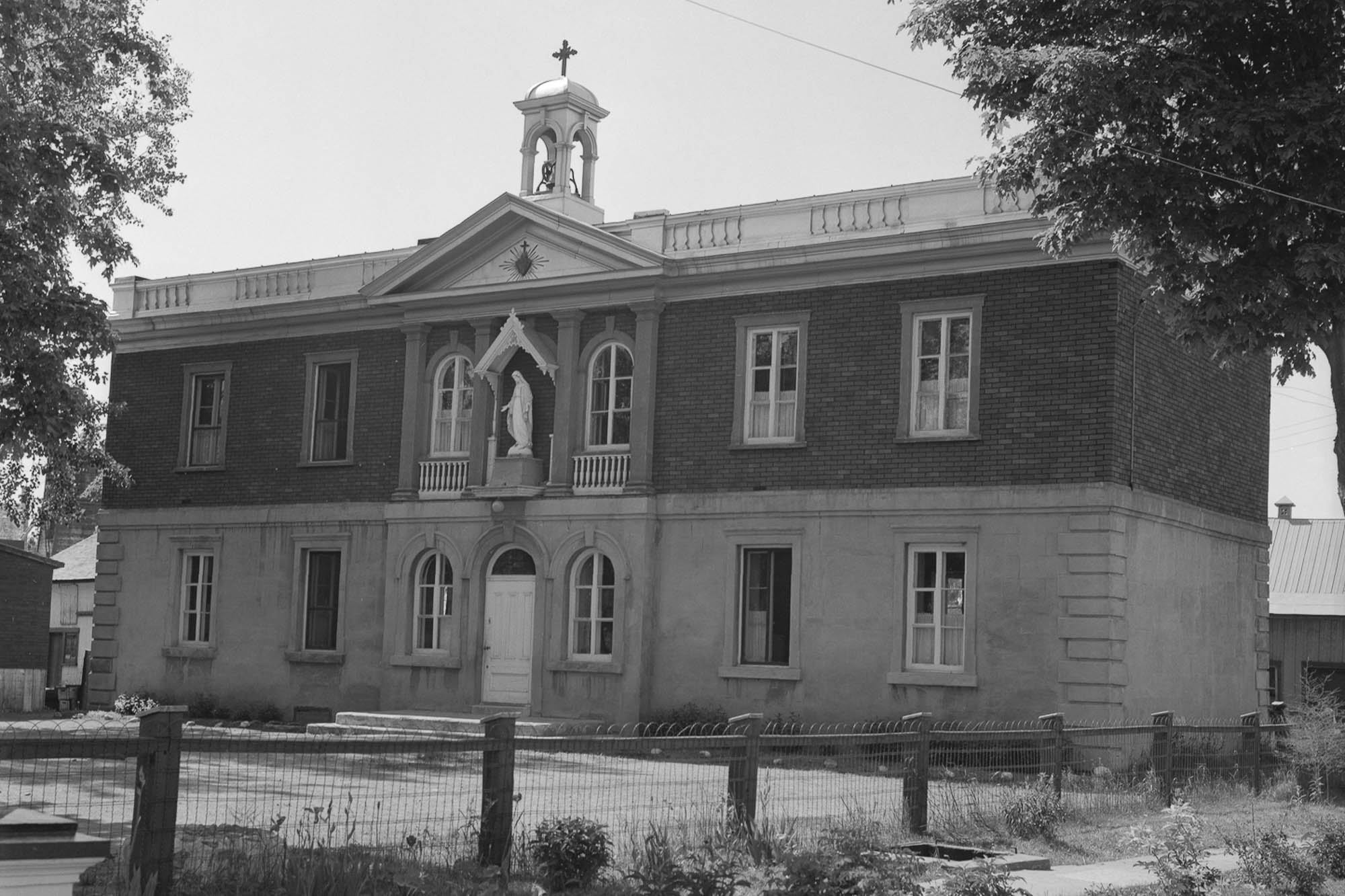 Archival black and white image of a stone and brick building with a neoclassical facade and a small bell tower.