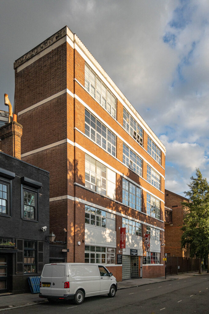 Exterior of a modern brick industrial facade with large rectangular windows. A white van is parked at the front.