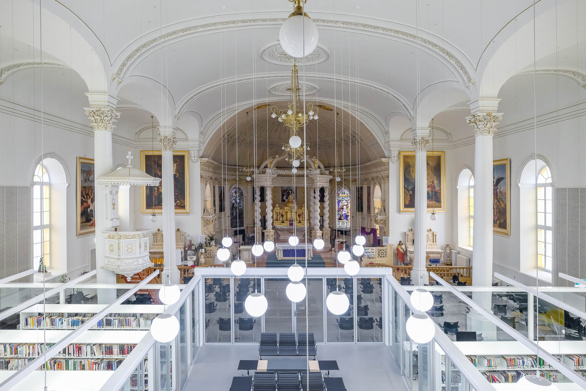 Interior of a church converted to a library. A glass enclosure containing the library is in the forefront, only occupying part of the church, which can be seen at the back.