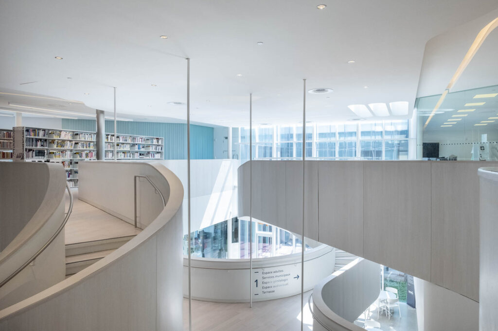 Interior of a contemporary library looking towards curving staircases and walkways, with bookshelves at the back.