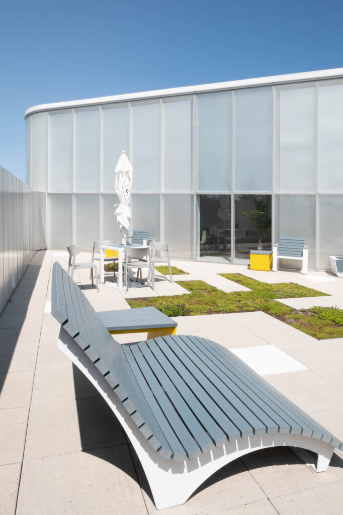Rooftop patio at a contemporary library with gently curving glass walls. On the patio are exterior furniture, a folded umbrella and moss planters.