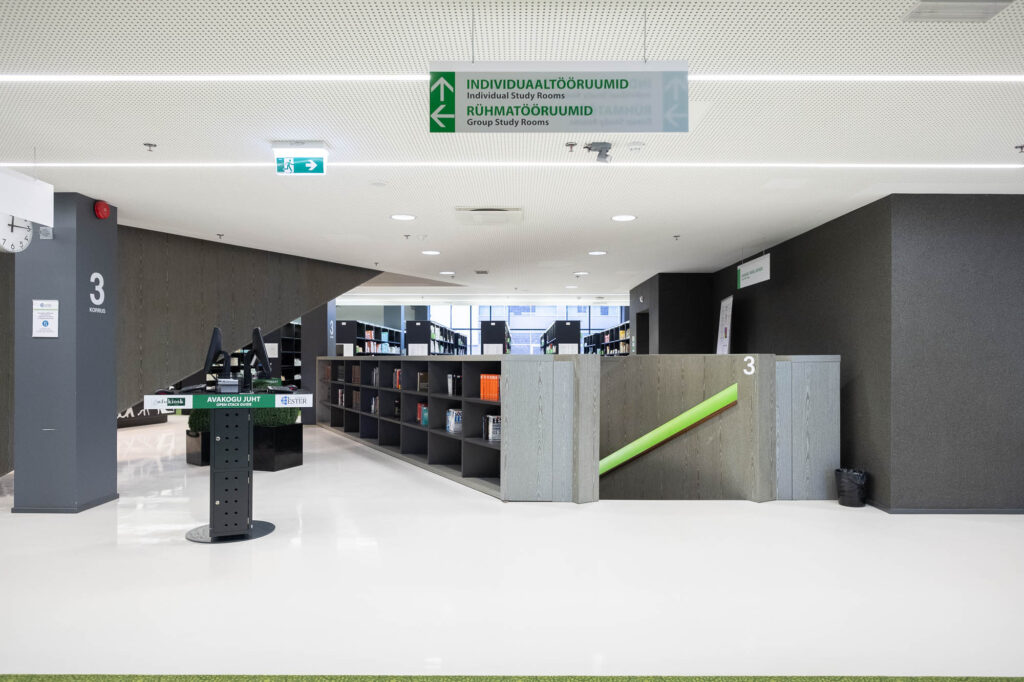 Interior of a contemporary library, showing the top of a staircase opening to a white and grey space with computers. A sign hanging from the ceiling reads "individual study rooms" and "group study rooms".