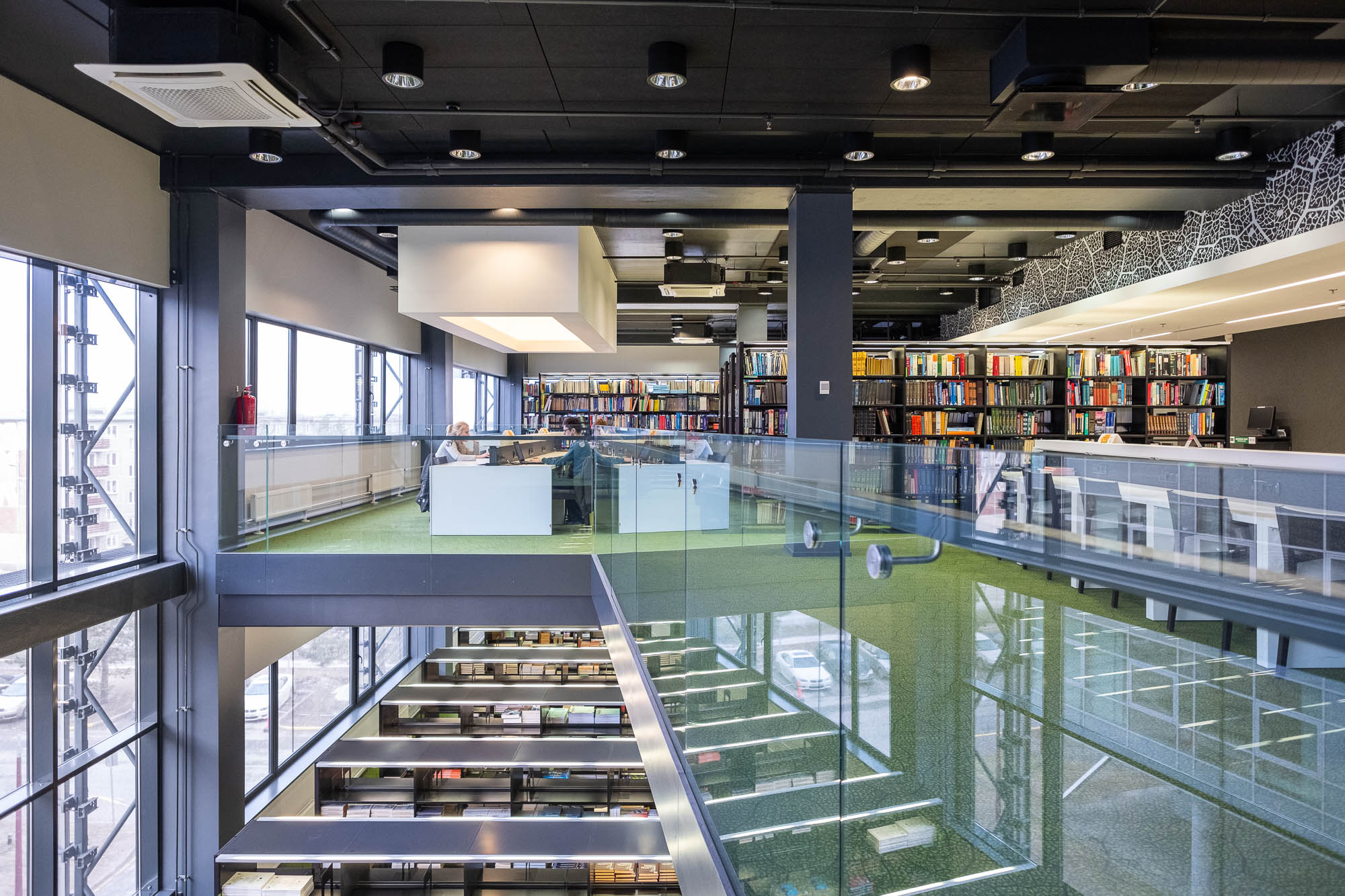 Interior of a contemporary library with rows of bookshelves on two levels connected by a lightwell.