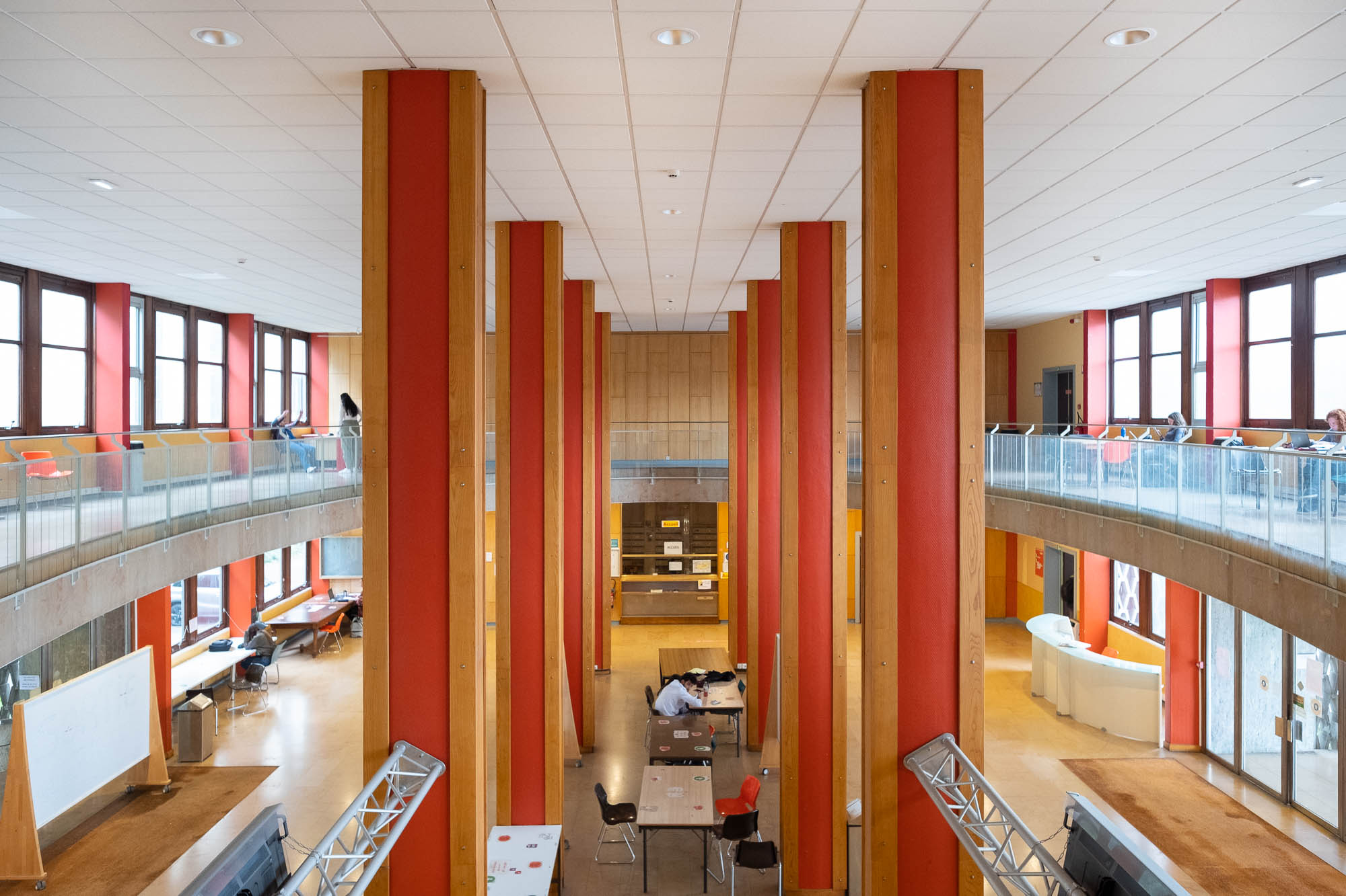 Interior of a modernist university building, with a large oval atrium pierced by eight square columns.