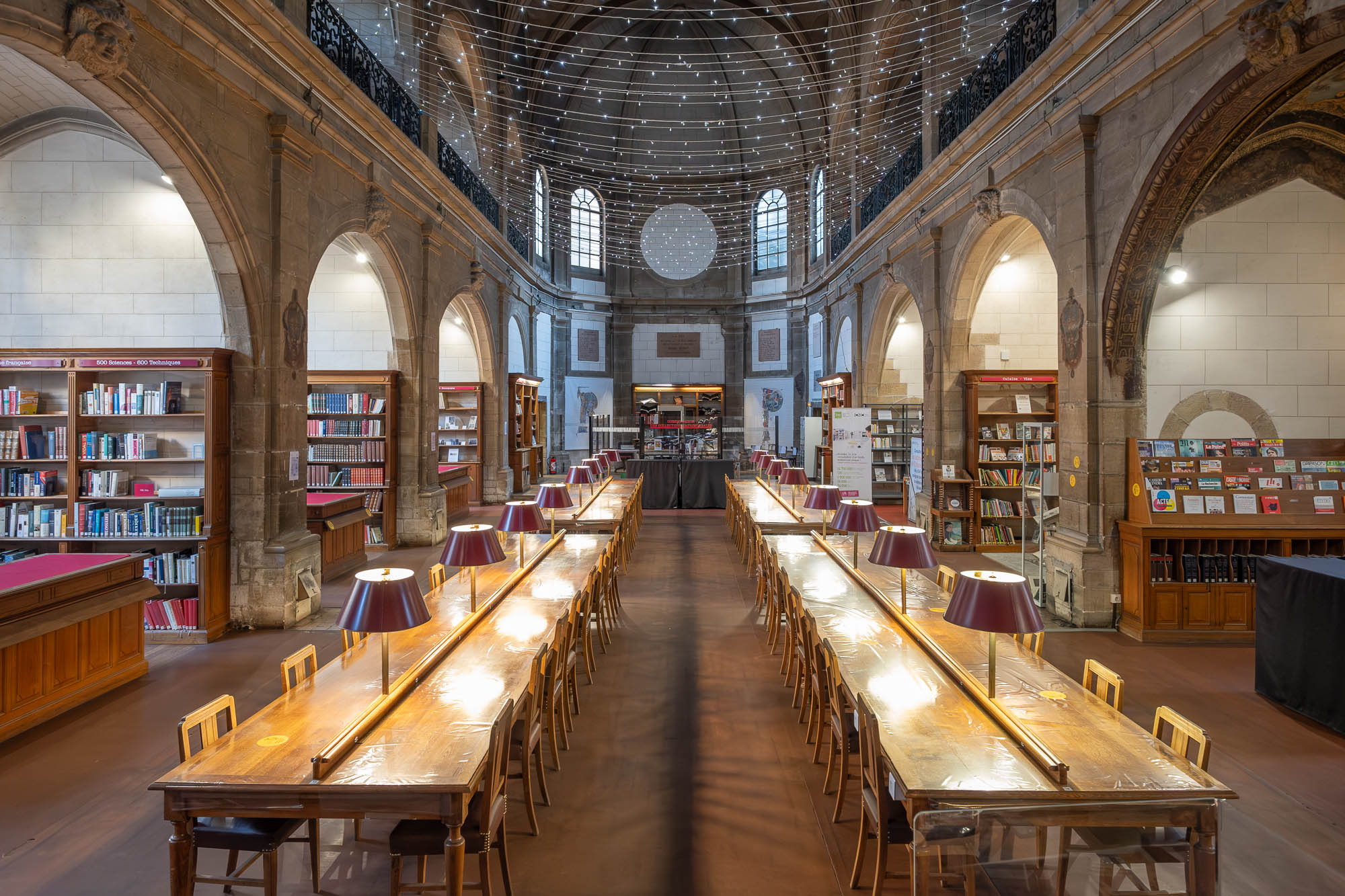 Interior of a church converted to a library. Long work tables are in the foreground. String lights hang from the ceiling.