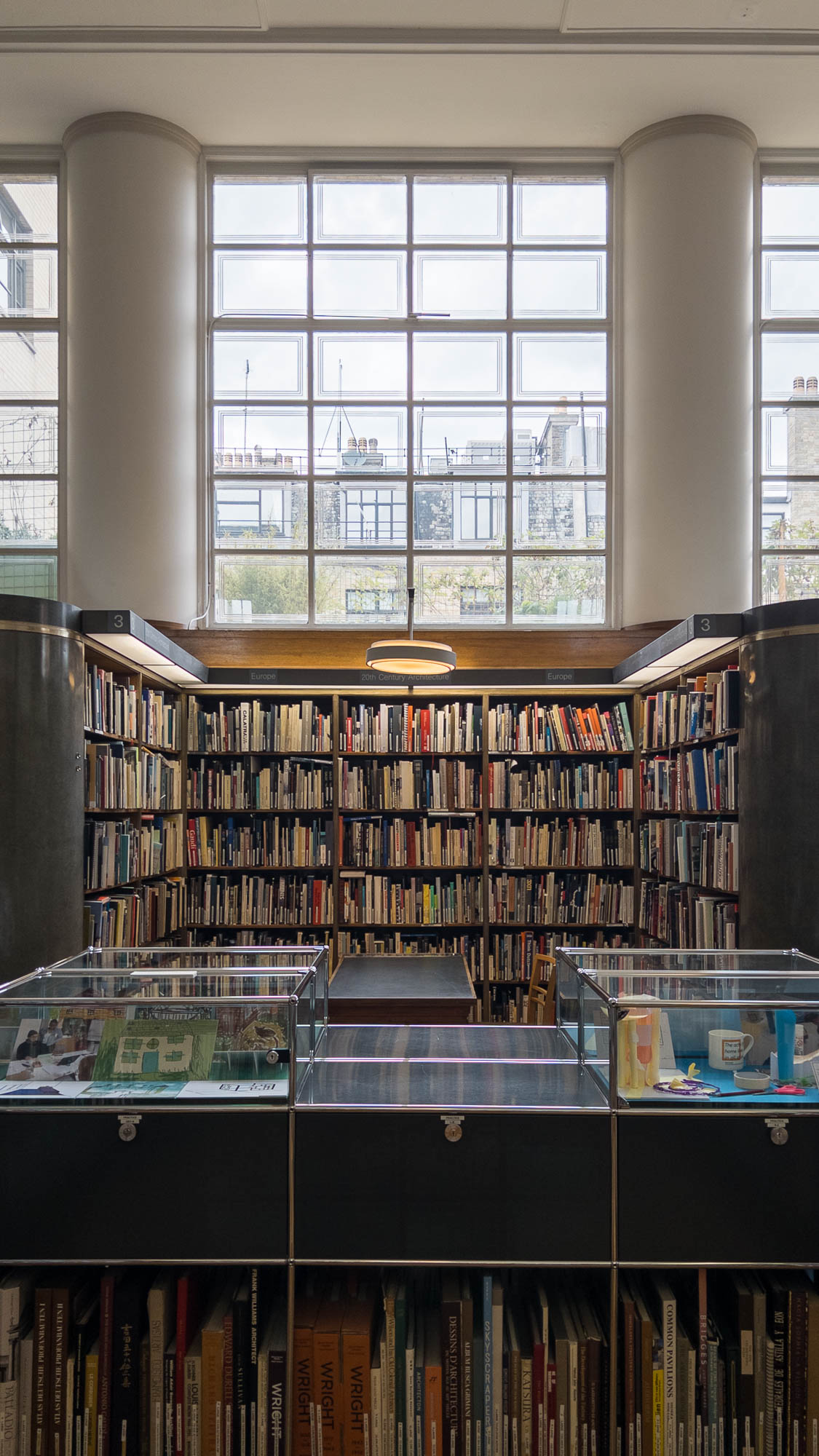 Interior of a library showing a book nook filled with bookshelves, with a row of windows above. In front are display cases with books underneath.