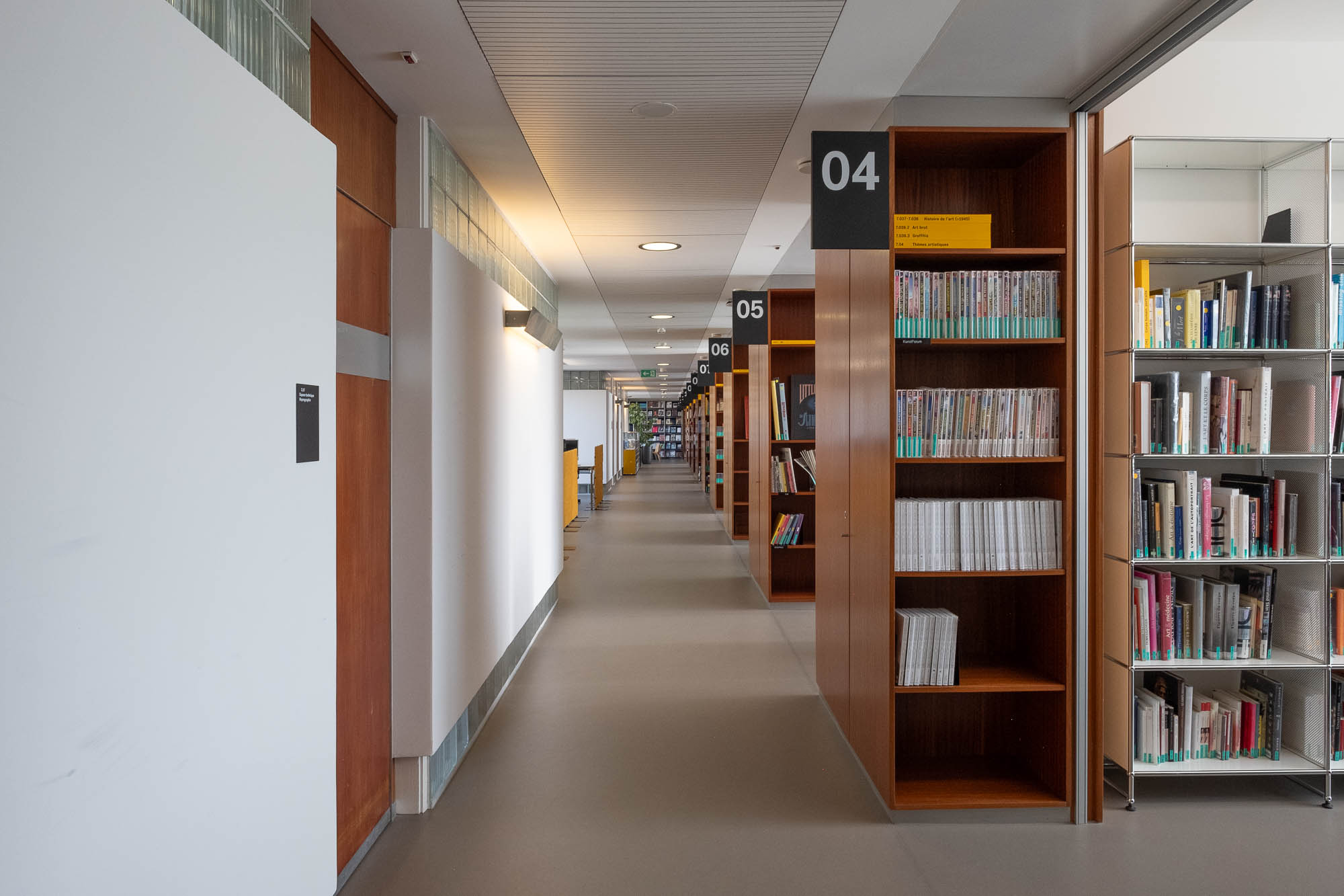 Interior of a library inside a former Modernist office building, with rows of bookshelves to the left.