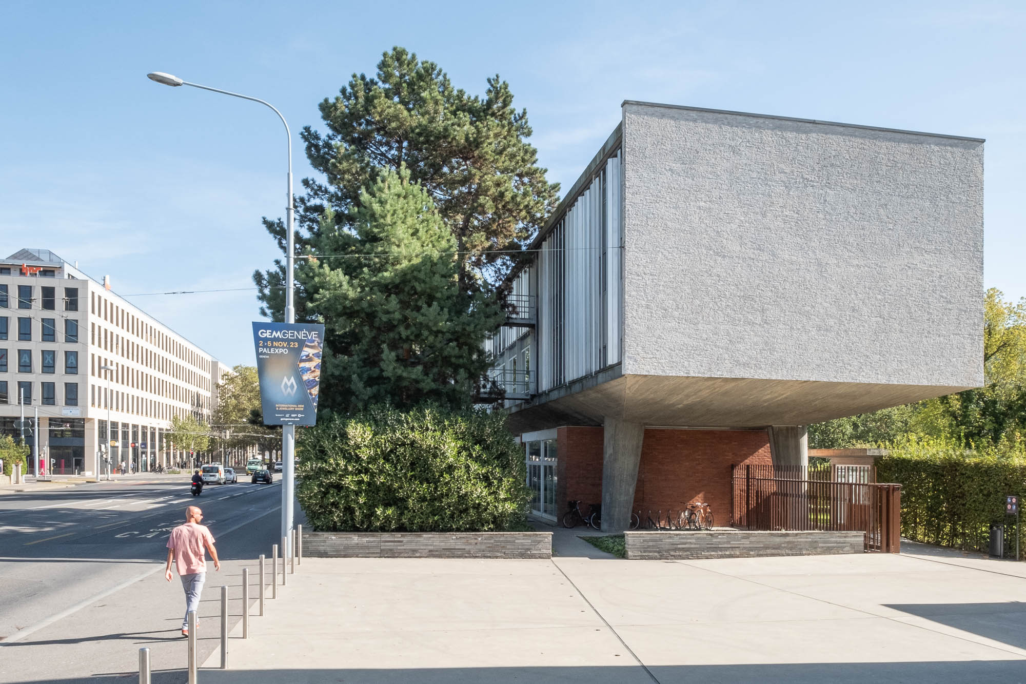 Exterior shot of a Modernist office block on stilts. To the left is a street where a man is walking.
