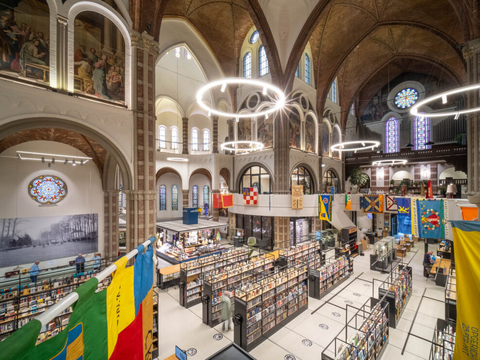 Interior of a brick church converted to a library with rows of contemporary bookshelves contrasting with the church interior. Flags are hanging from a curved mezzanine wrapping around the space.