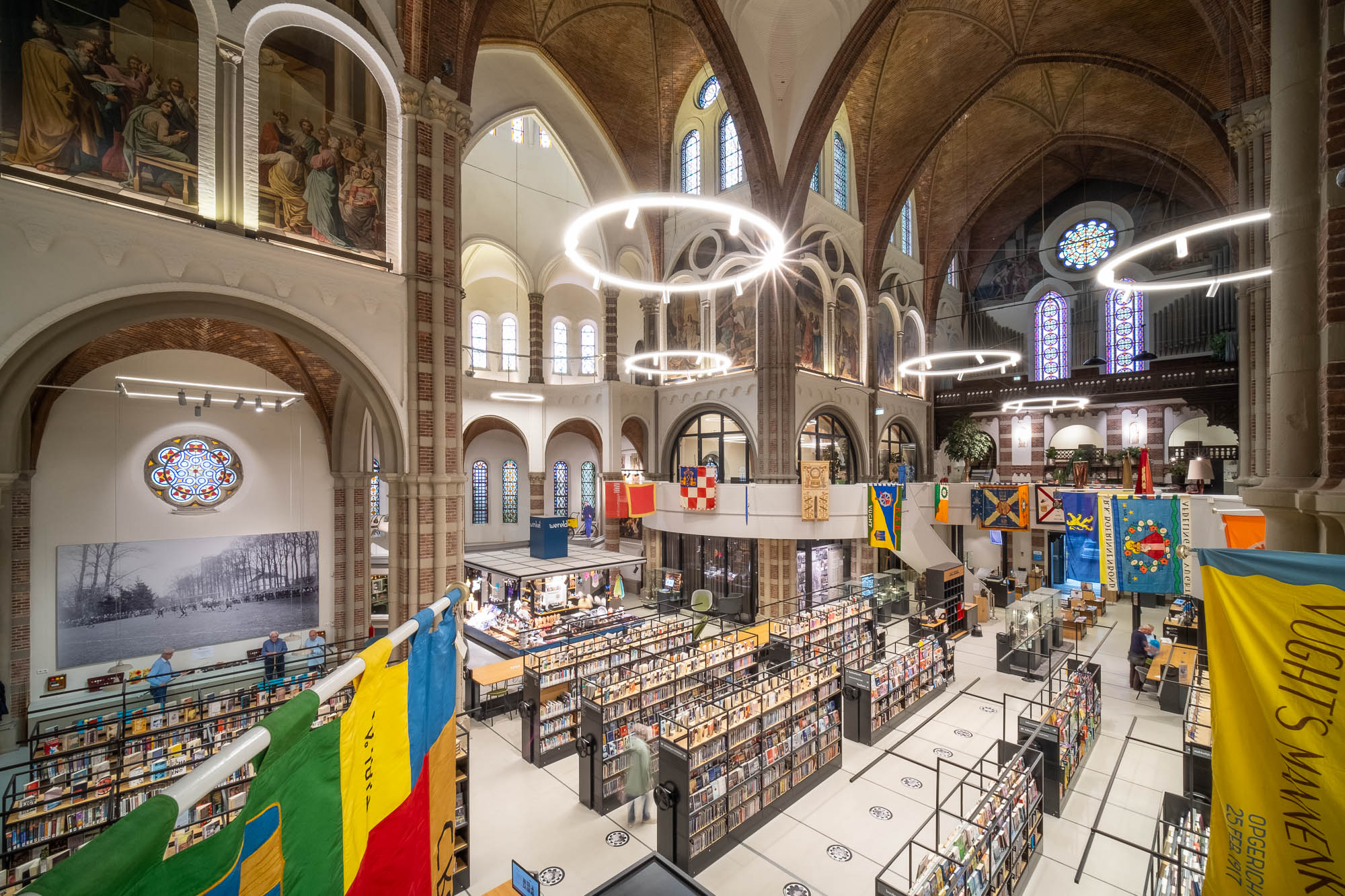 Interior of a brick church converted to a library with rows of contemporary bookshelves contrasting with the church interior. Flags are hanging from a curved mezzanine wrapping around the space.