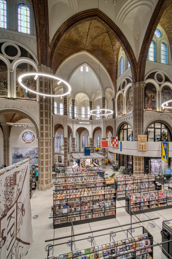 Interior of a brick church converted to a library with rows of contemporary bookshelves contrasting with the church interior. Flags are hanging from a curved mezzanine wrapping around the space.