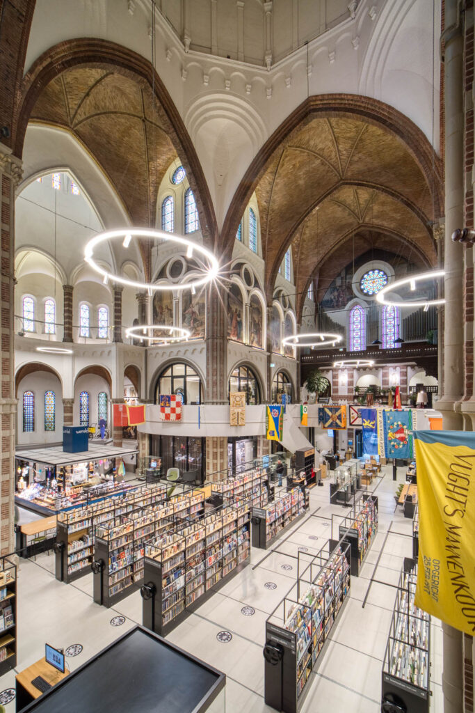 Interior of a brick church converted to a library with rows of contemporary bookshelves contrasting with the church interior. Flags are hanging from a curved mezzanine wrapping around the space.