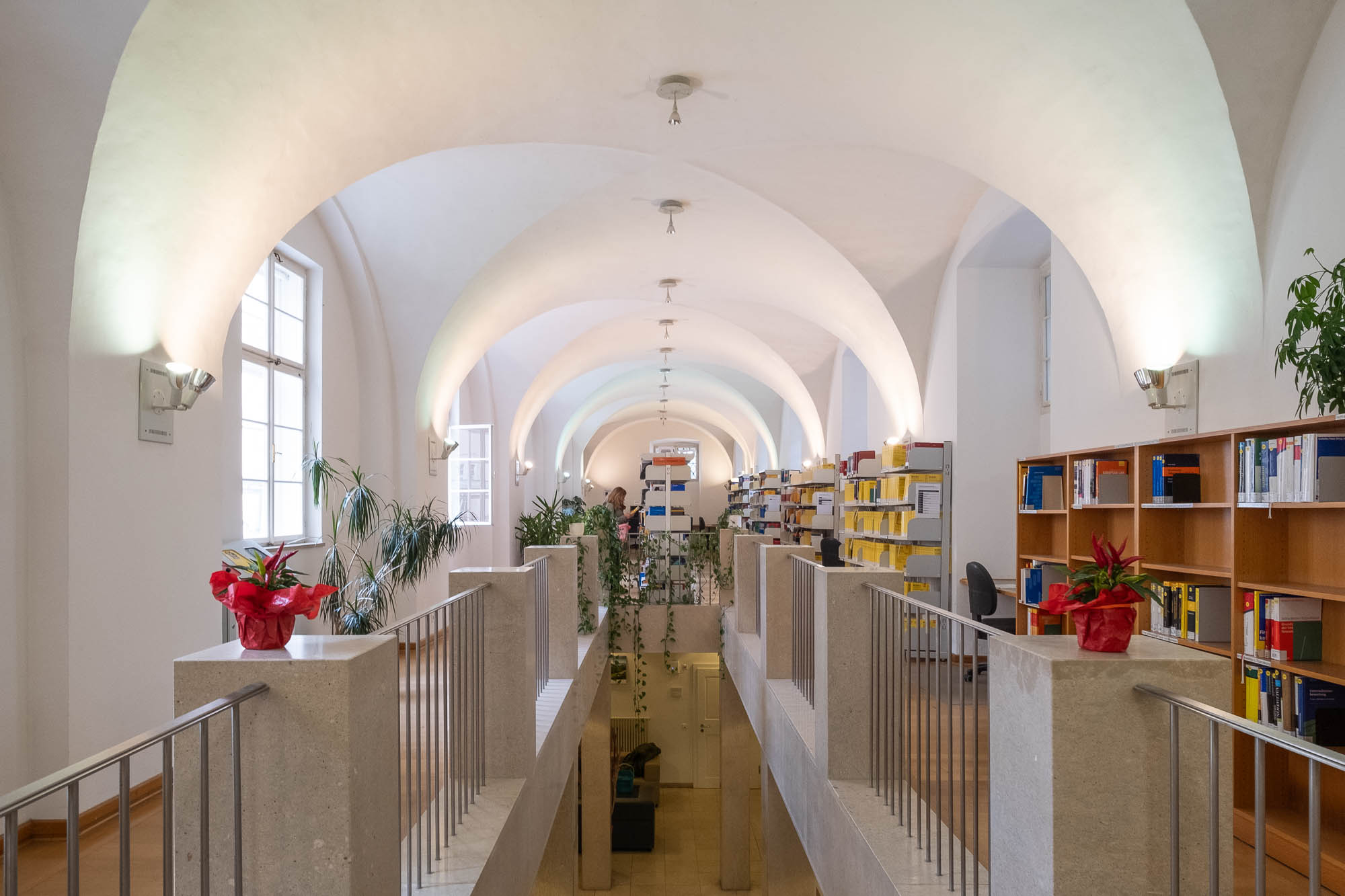Interior of a library inside a Renaissance palazzo, a rectangular vaulted space with a contemporary staircase in the centre. Bookshelves line the walls.