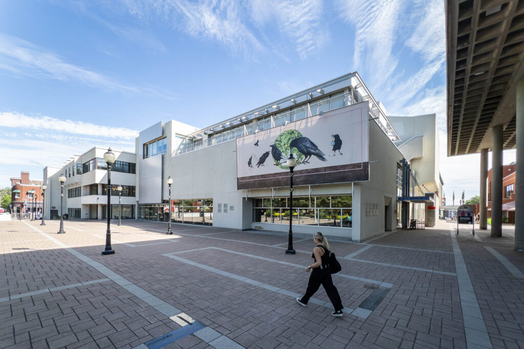 Exterior view of a civic plaza with a group of modernist buildings. A woman is walking in the forefront.